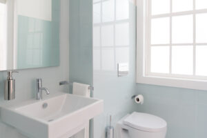 small bathroom with natural lighting from window, light blue walls, and mirror above the sink