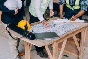 commercial renovation contractors looking at plans on wooden table with yellow construction hardhat