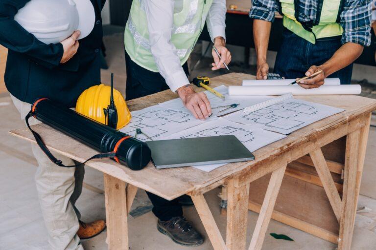 commercial renovation contractors looking at plans on wooden table with yellow construction hardhat