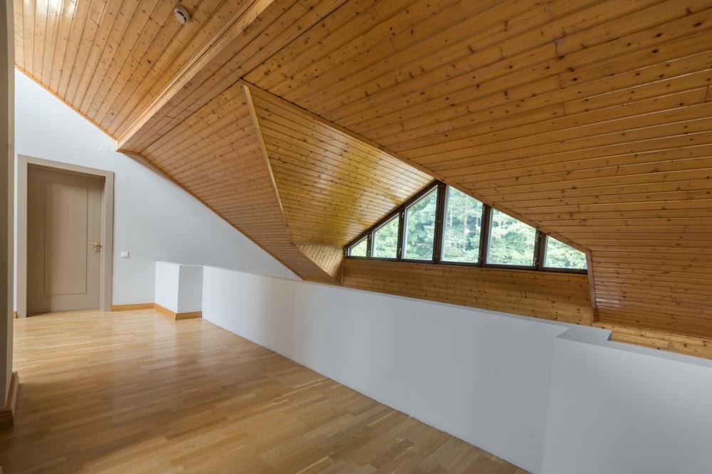 A bright attic decorated with natural wood in a country house. Triangular window with a view of a dense forest on a sunny day.