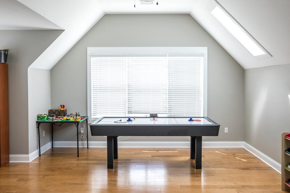Open and airy upstairs loft game room near a window under an attic style ceiling with a window for natural light and hardwood floors