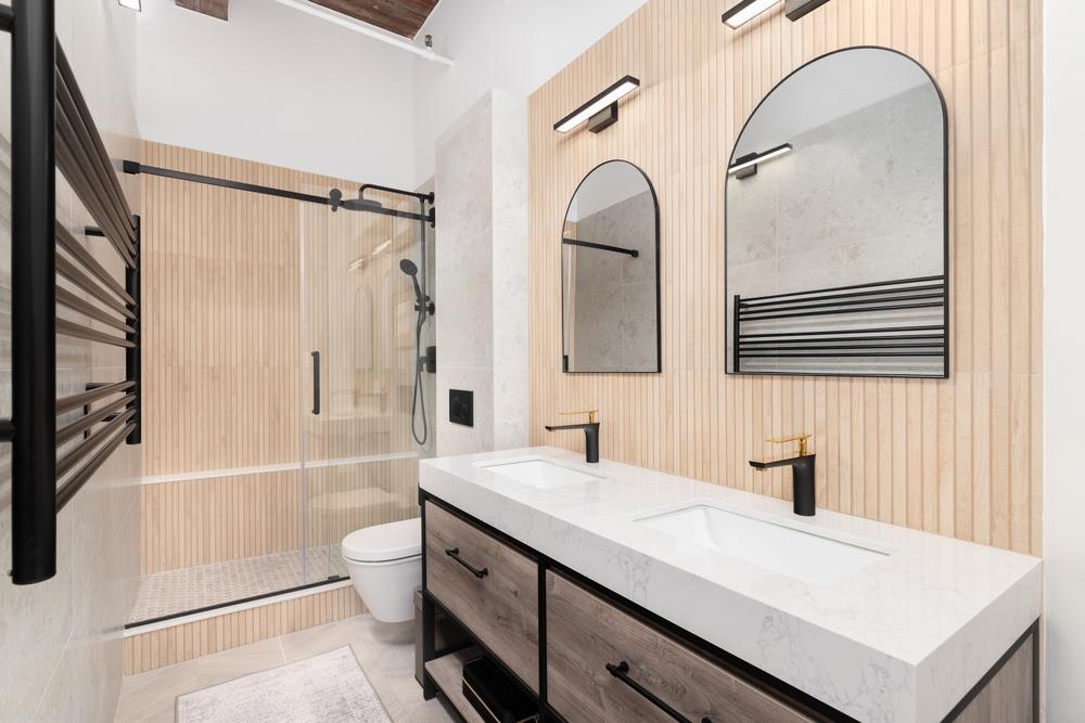 A bathroom with a wood slat accent wall, a marble slab countertop on a black and wood cabinet